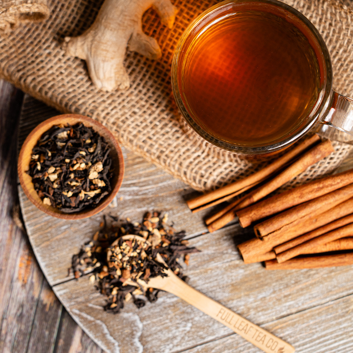 Organic Skinny Natural Tea in a glass mug surrounded by cinnamon sticks, ginger root, and loose leaf tea on a rustic wooden surface.