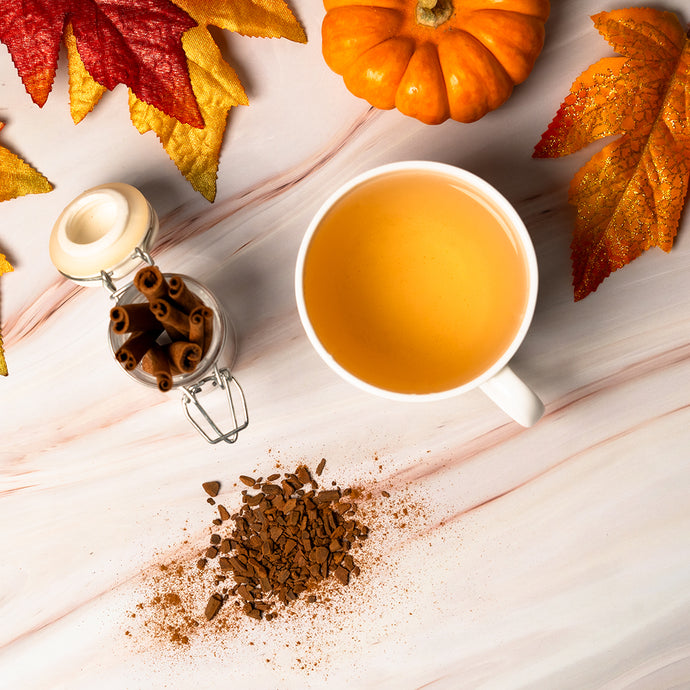 Cup of tea with cinnamon, pumpkins, and autumn leaves on a wooden surface