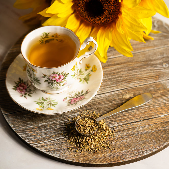 Teacup with tea, sunflower, and spoonful of dried oregano on a wooden surface