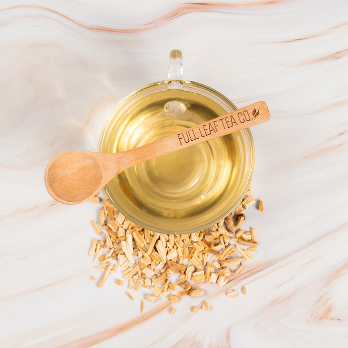 Glass teacup filled with shatavari tea, with a wooden spoon and tea leaves on a light background