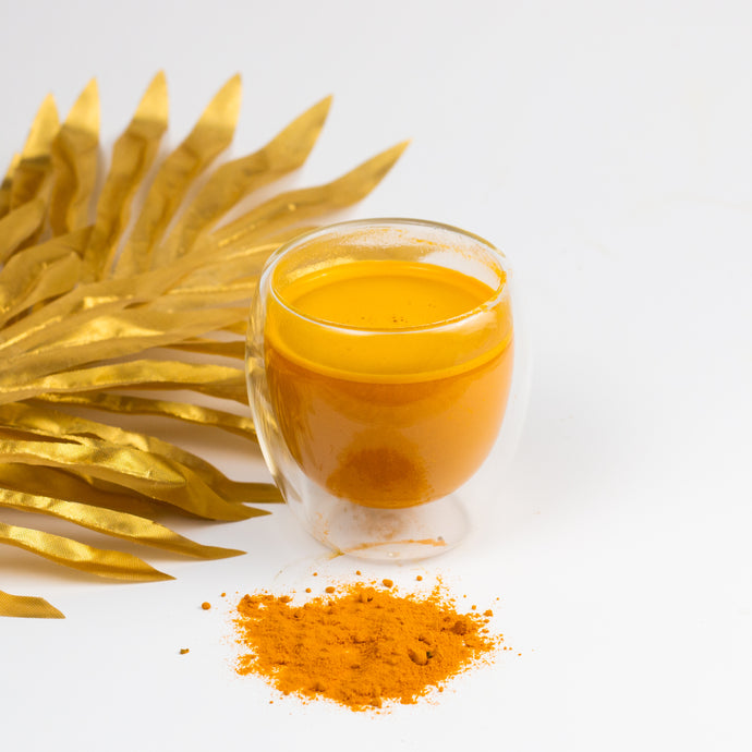 Glass of turmeric tea next to turmeric powder and golden leaves on a white background