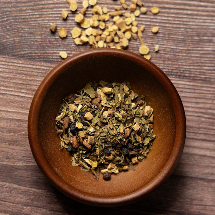 Herbal tea leaves in a brown ceramic bowl on a wooden surface