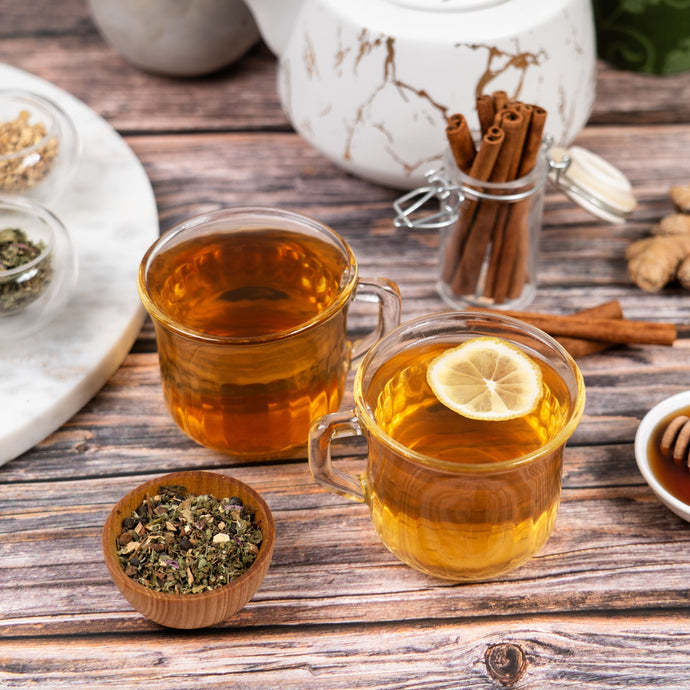 Two glasses of tea with lemon slices on a wooden table with tea-making ingredients.