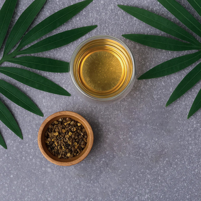 Glass of liquid with a wooden bowl of herbs on a gray surface with green leaves.