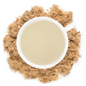 White mug filled with Slippery Elm Tea with slippery elm herb around the cup.