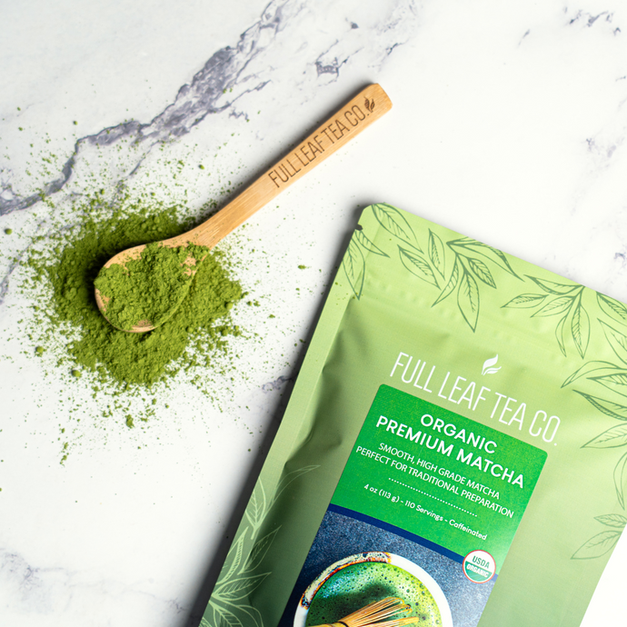 Full Leaf Tea Co. Organic Premium Matcha pouch with a wooden spoon of vibrant green matcha powder on a marble surface.
