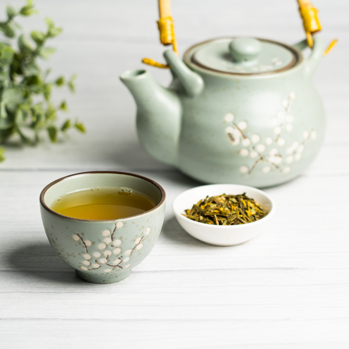 Cup of Organic Joint Health Tea in a floral-patterned ceramic teacup with matching teapot and a bowl of loose herbal tea leaves on a light wooden surface.