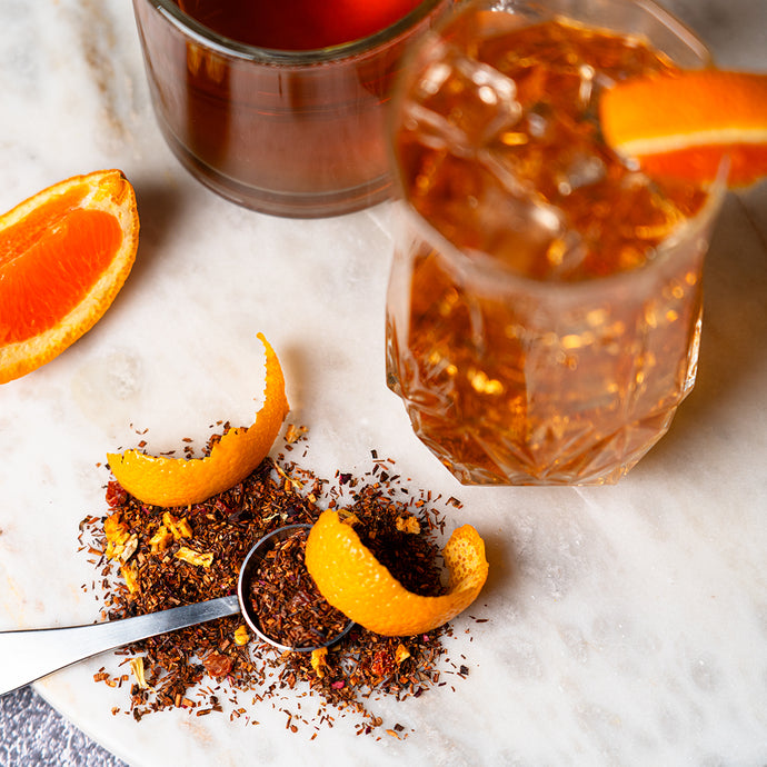Organic Blood Orange Rooibos tea with orange slices, zest, and loose tea leaves on a marble surface.