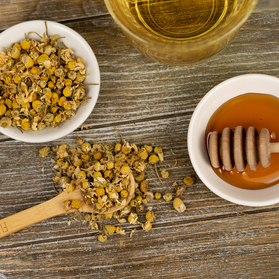 Organic Bladder Health Tea with dried chamomile flowers, honey, and a cup of brewed tea on a rustic wooden surface.