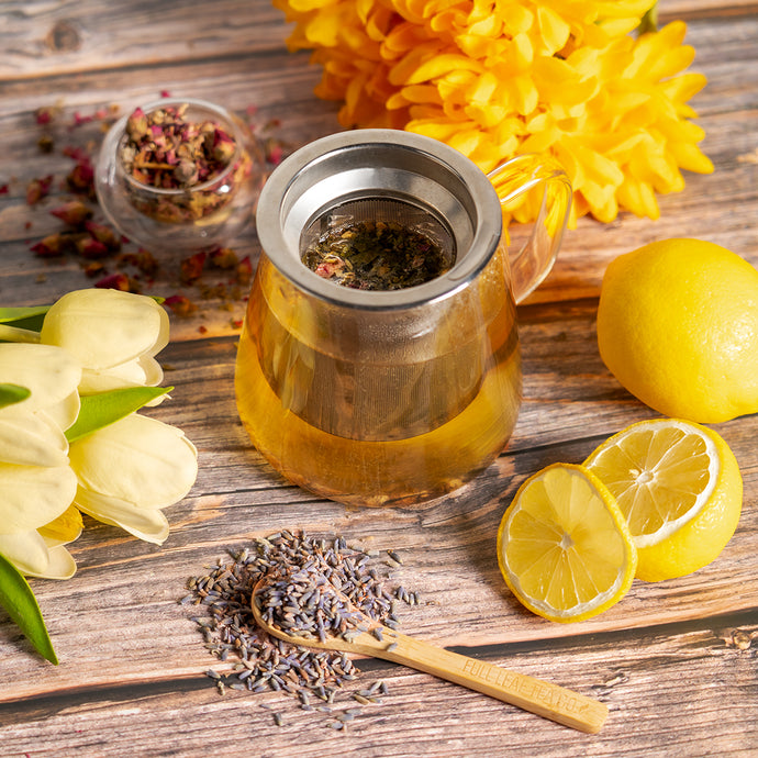 Tea infuser with loose leaf tea leaves on a wooden surface with lemons and flowers.