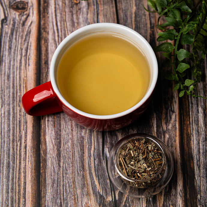 Red mug with epimedium tea on a wooden surface, accompanied by a small bowl of loose tea leaves.