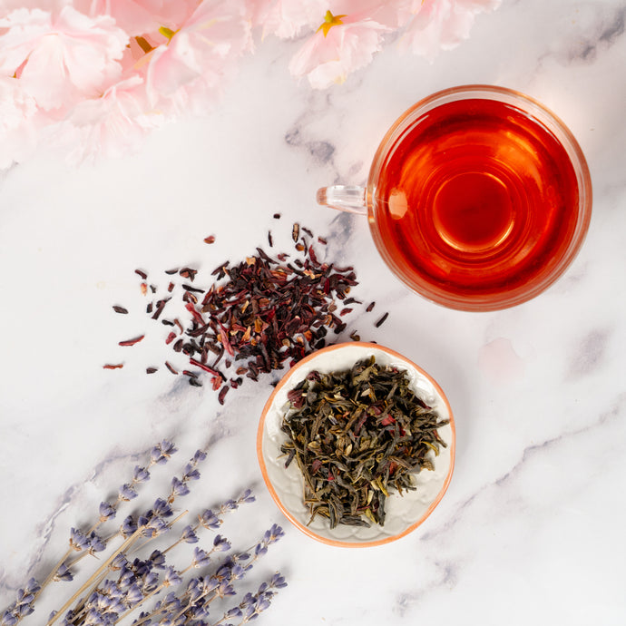 Tea leaves, a cup of tea, and flowers on a marble surface