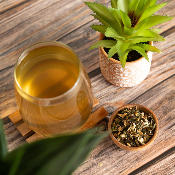 Glass of tea with a bowl of tea leaves and a potted plant on a wooden surface
