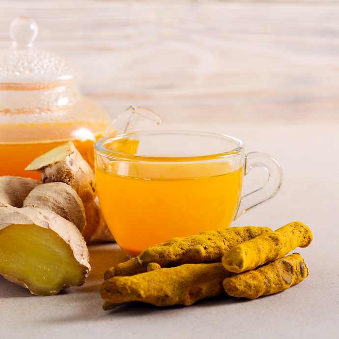 Glass cup of turmeric tea with turmeric roots and a teapot on a light background