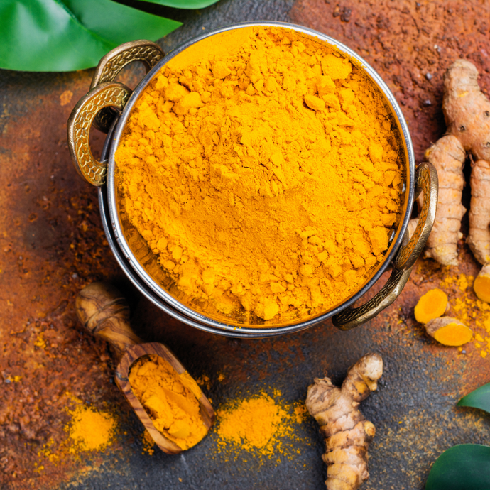 Turmeric powder in a metal container with turmeric roots on a rustic surface
