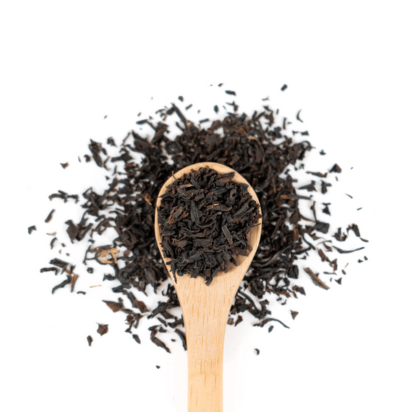 A wooden spoon filled with english breakfast tea leaves surrounded by tea leaves on a white background. 