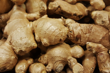 Close-up of fresh whole ginger roots with light brown skin piled together.
