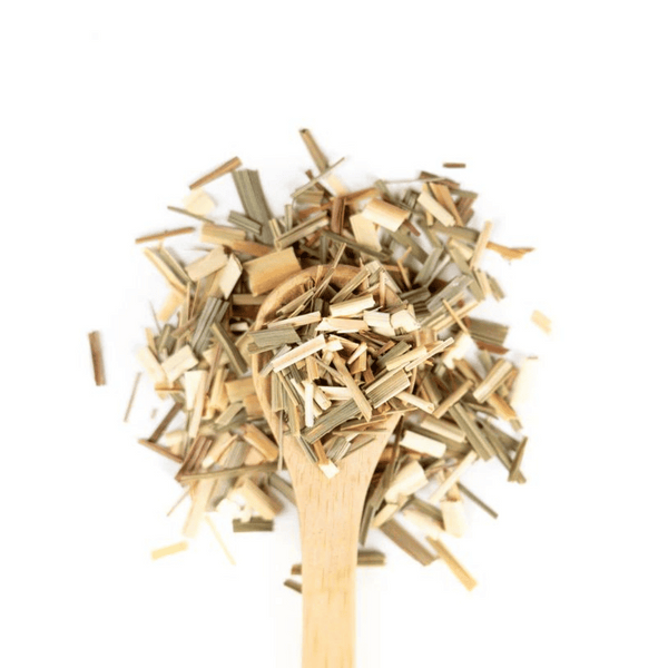 A white spoon filled with and surrounded by lemongrass on a white background. 